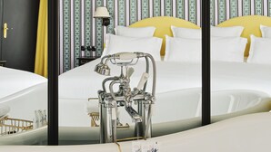 Una cama con dosel con sábanas blancas, un espejo con detalles dorados y una mesita de noche con lámpara.