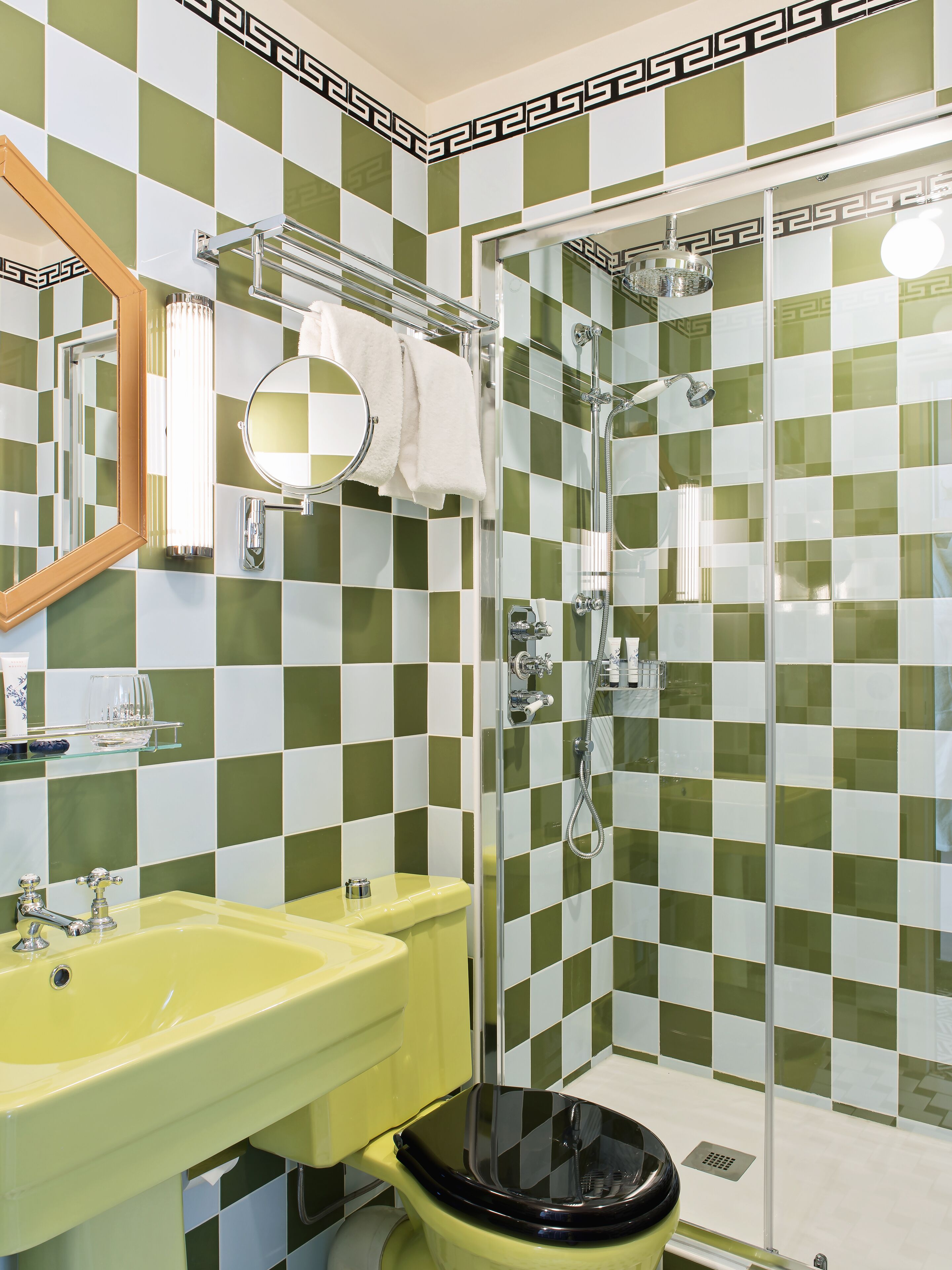 A bathroom with a yellow sink, a toilet, a shower with a glass door, and green and white checkered tiles.