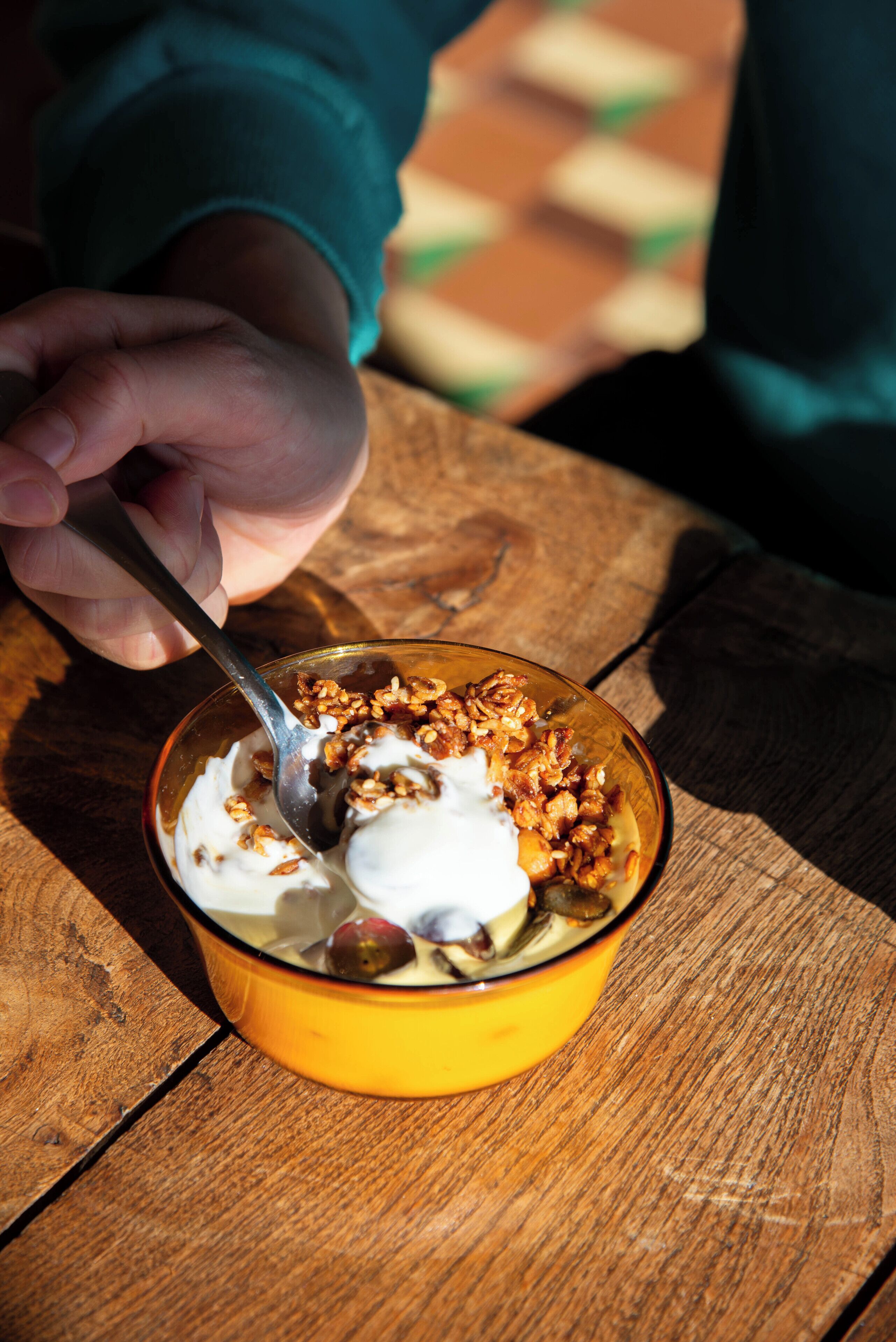 A bowl of yogurt with granola and fruit on a wooden table.