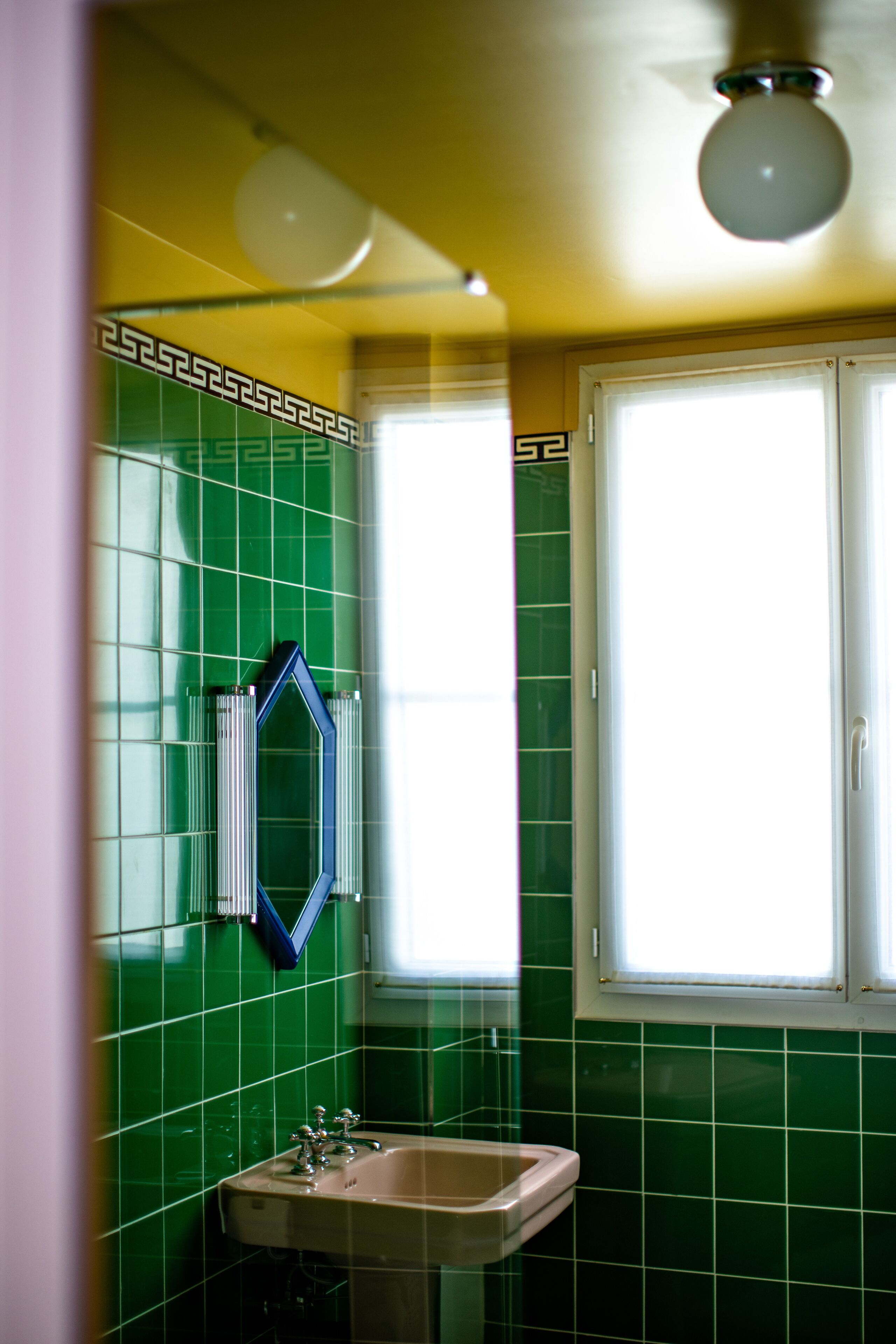 A bathroom with green tiles, a sink, and a window with white frames.