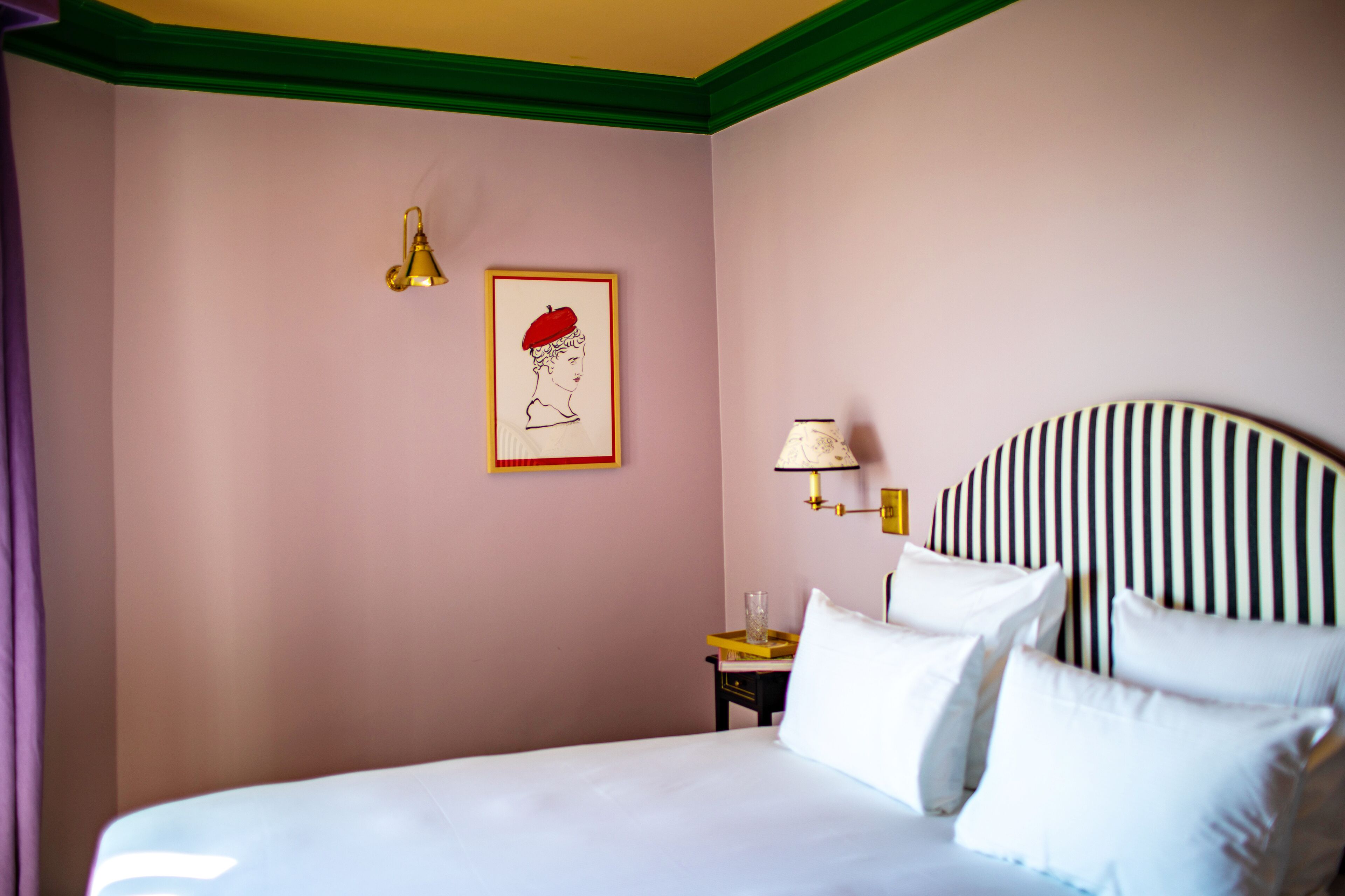 Une chambre d’hôtel comprenant un lit, une table de chevet, une lampe, un tableau encadré et un luminaire fixé au mur.