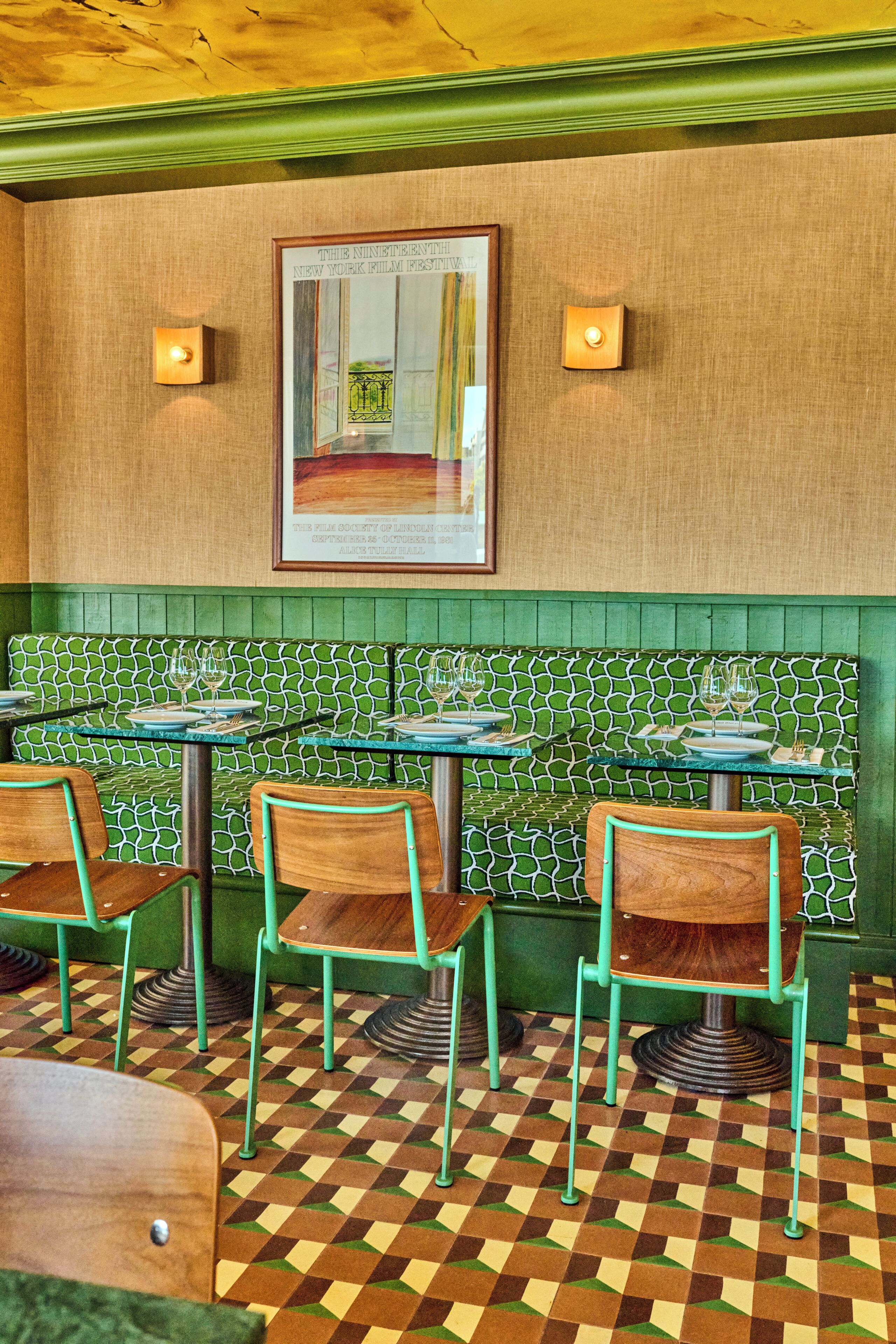 Interior de restaurante com assentos em cabines com padrão verde, cadeiras de madeira e piso xadrez.