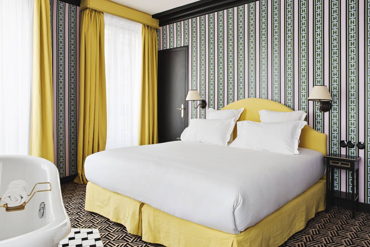 Une chambre d’hôtel avec un grand lit, une baignoire blanche et un papier peint à motifs.