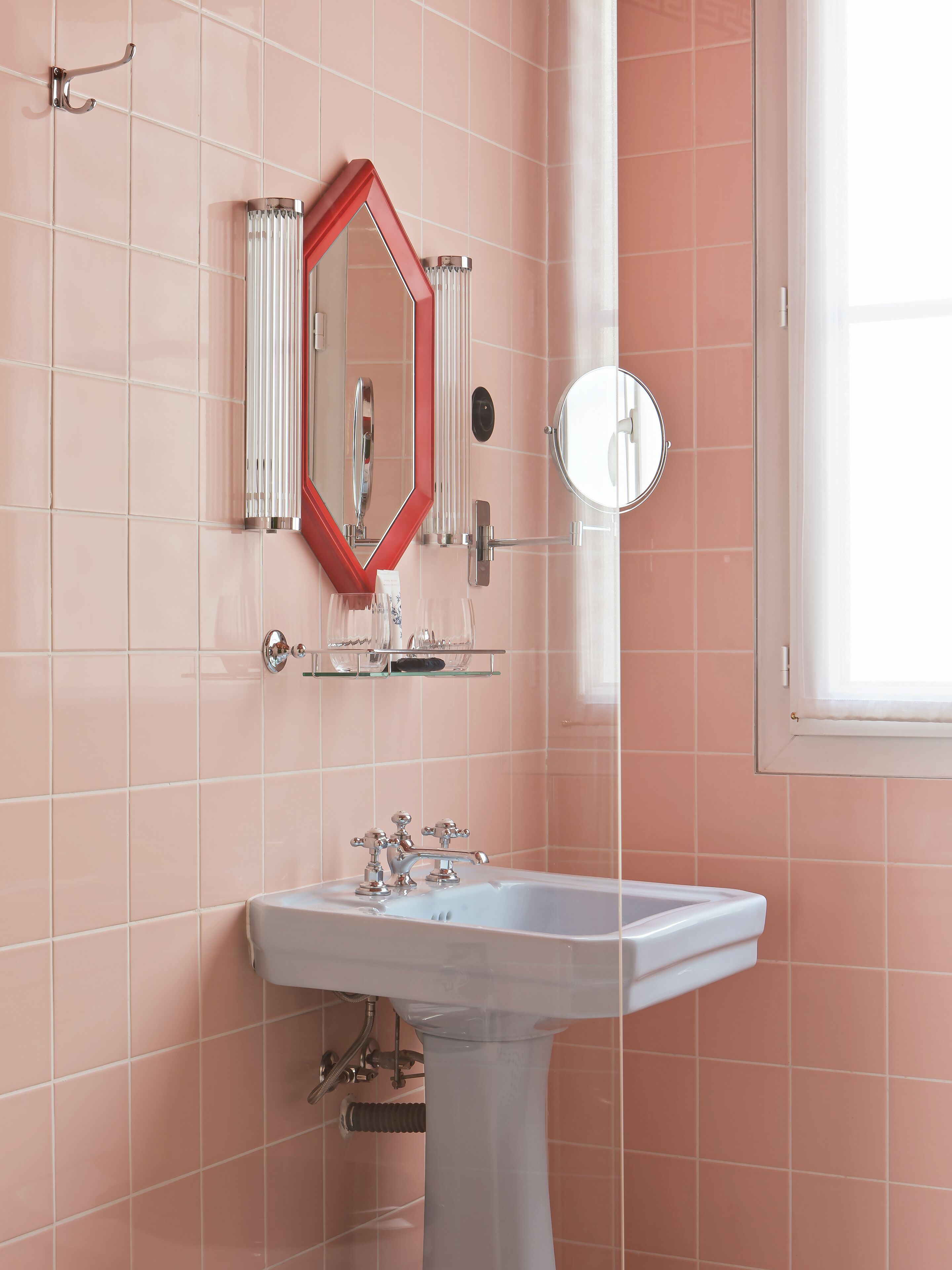 A bathroom with a white sink, a red-framed mirror, and pink tiled walls.