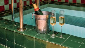 Zona de bar con pared de baldosas a cuadros, un taburete de cobre, un cubo con una botella y dos copas de champán.