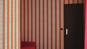 A room with a patterned wallpaper, a red sofa, a small table with books, and a black door.