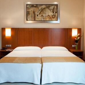 Ein Doppelbett mit Holz-Kopfteil, zwei Nachttische mit Lampen, ein gerahmtes abstraktes Gemälde über dem Bett und ein Blumenarrangement auf einem der Tische.