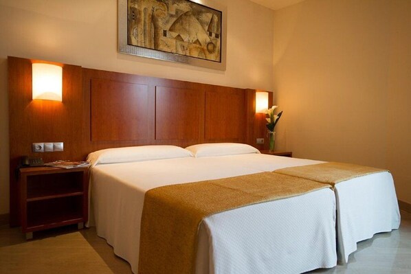 A hotel room with a large bed, wooden headboard, bedside lamps, and a painting on the wall. - Leflet Valme (Dos Hermanas)