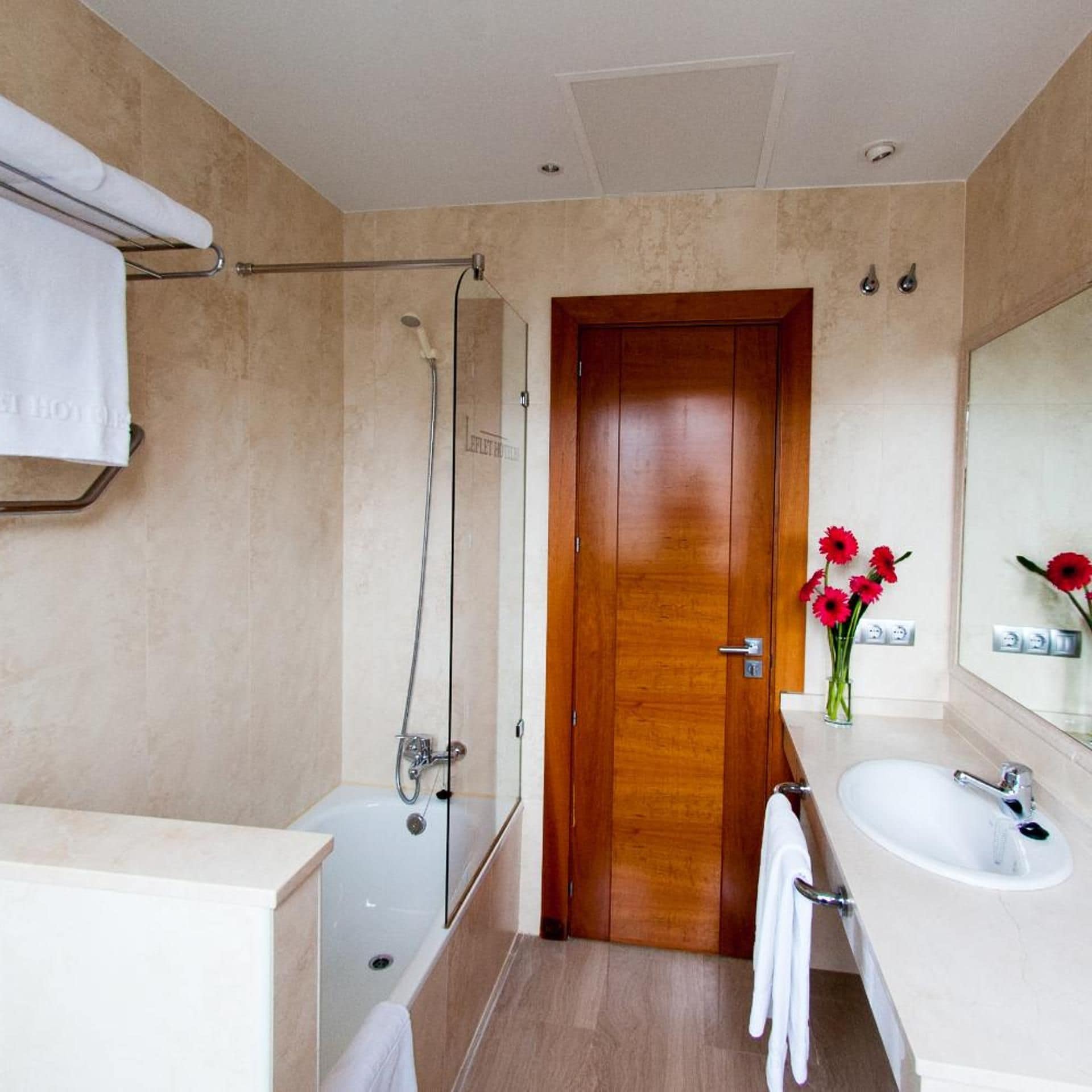A bathroom with a shower, a wooden door, a sink, and a mirror.