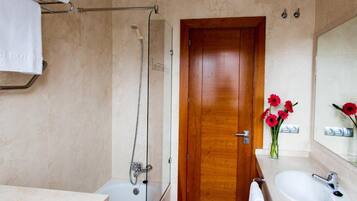 A bathroom with a shower, a wooden door, a sink, and a mirror.