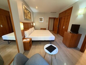 A hotel room with a bed, bedside tables, a desk, a chair, a TV, and wooden wardrobes. - Leflet Valme (Dos Hermanas)
