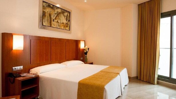 Habitación de hotel con una cama grande, mesitas de noche, un cuadro en la pared y una ventana con cortinas.