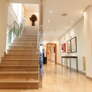 A staircase leading to a higher floor, a reception desk, and framed artwork on the wall. - Leflet Valme (Dos Hermanas)