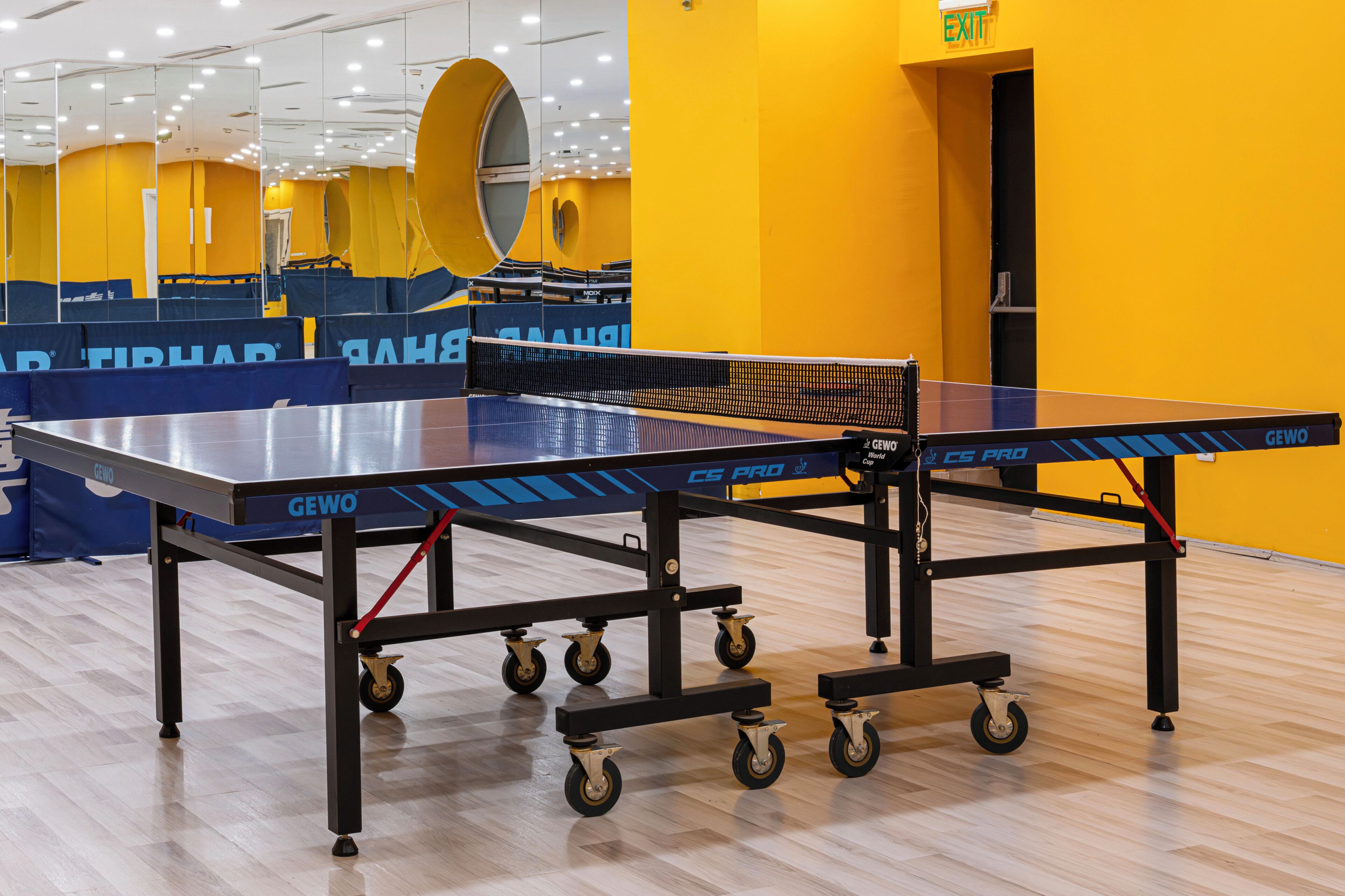 A ping pong table with wheels in a room with yellow walls and a large mirror.