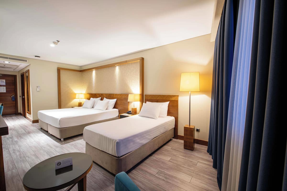 A hotel room with two beds, a desk, a chair, and a lamp.