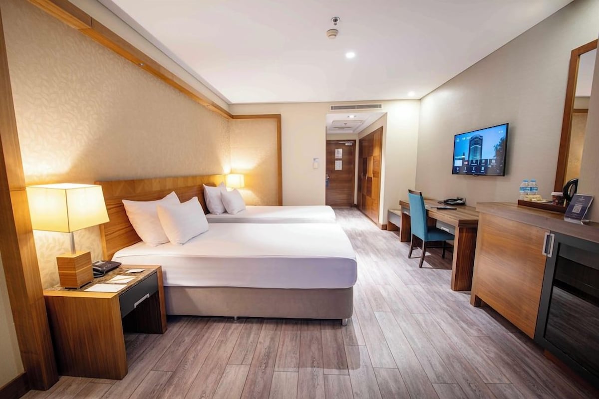 A hotel room with a bed, bedside table, lamp, desk, chair, and a television.