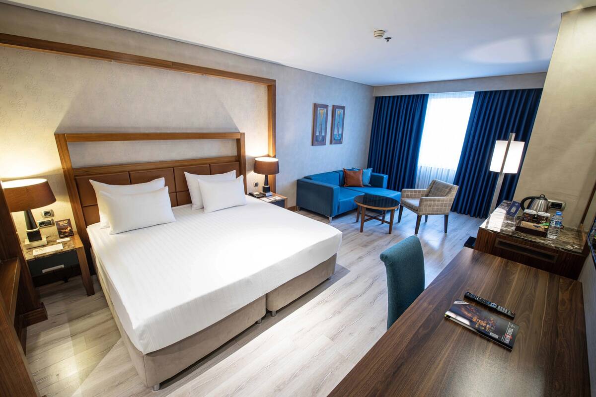 A hotel room with a large bed, a sofa, a desk, and a chair.