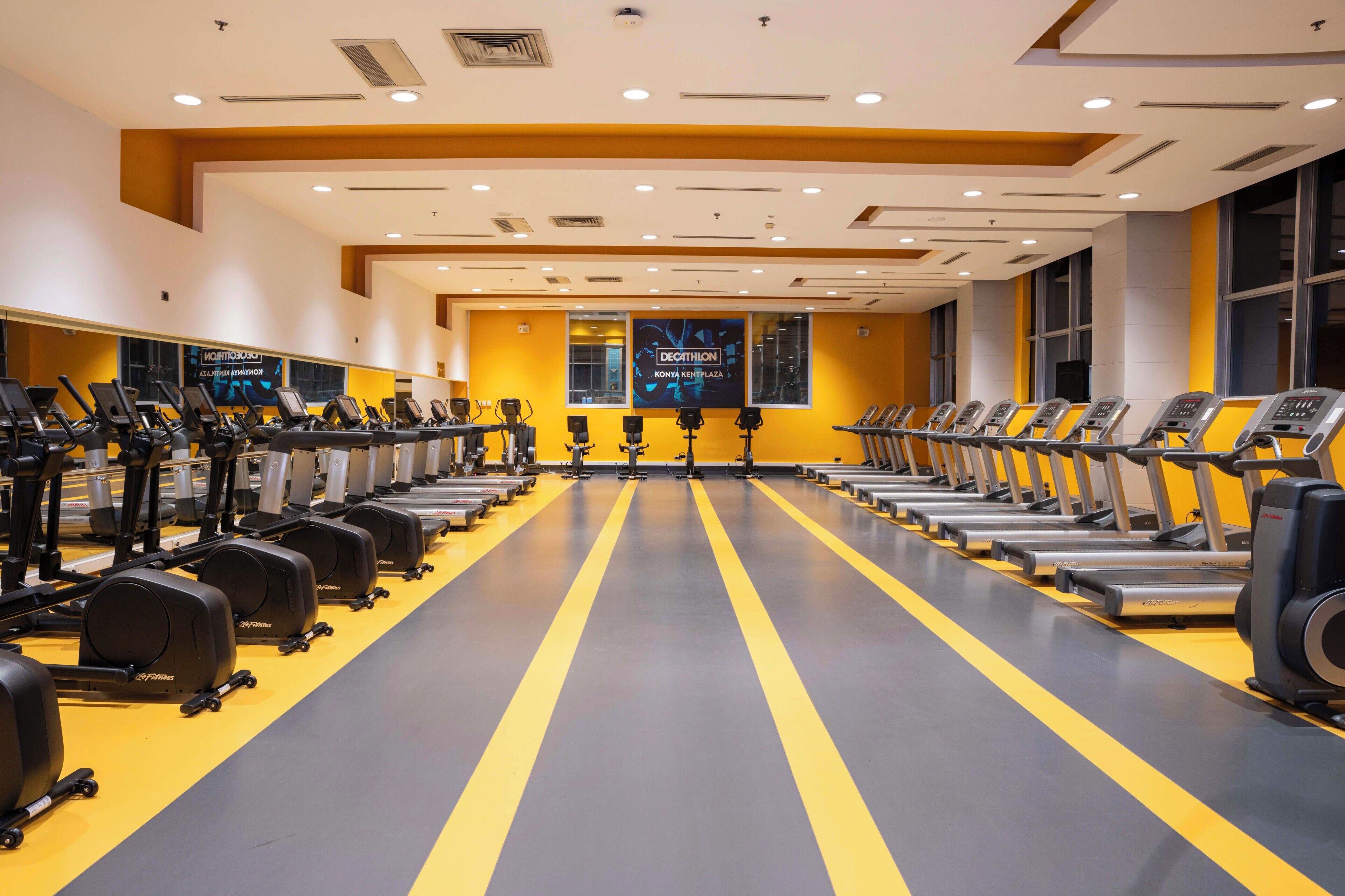 A gym with treadmills, stationary bikes, and weight machines arranged in rows.