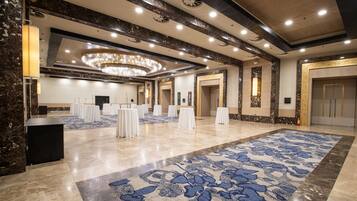 A spacious hotel lobby with a large patterned carpet, marble flooring, and a grand chandelier.