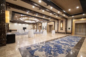 A spacious hotel lobby with a large patterned carpet, marble flooring, and a grand chandelier.
