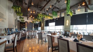 A spacious dining area with multiple tables and chairs, hanging plants, and pendant lighting. - Dedeman Konya Hotel And Convention Center (Konya)