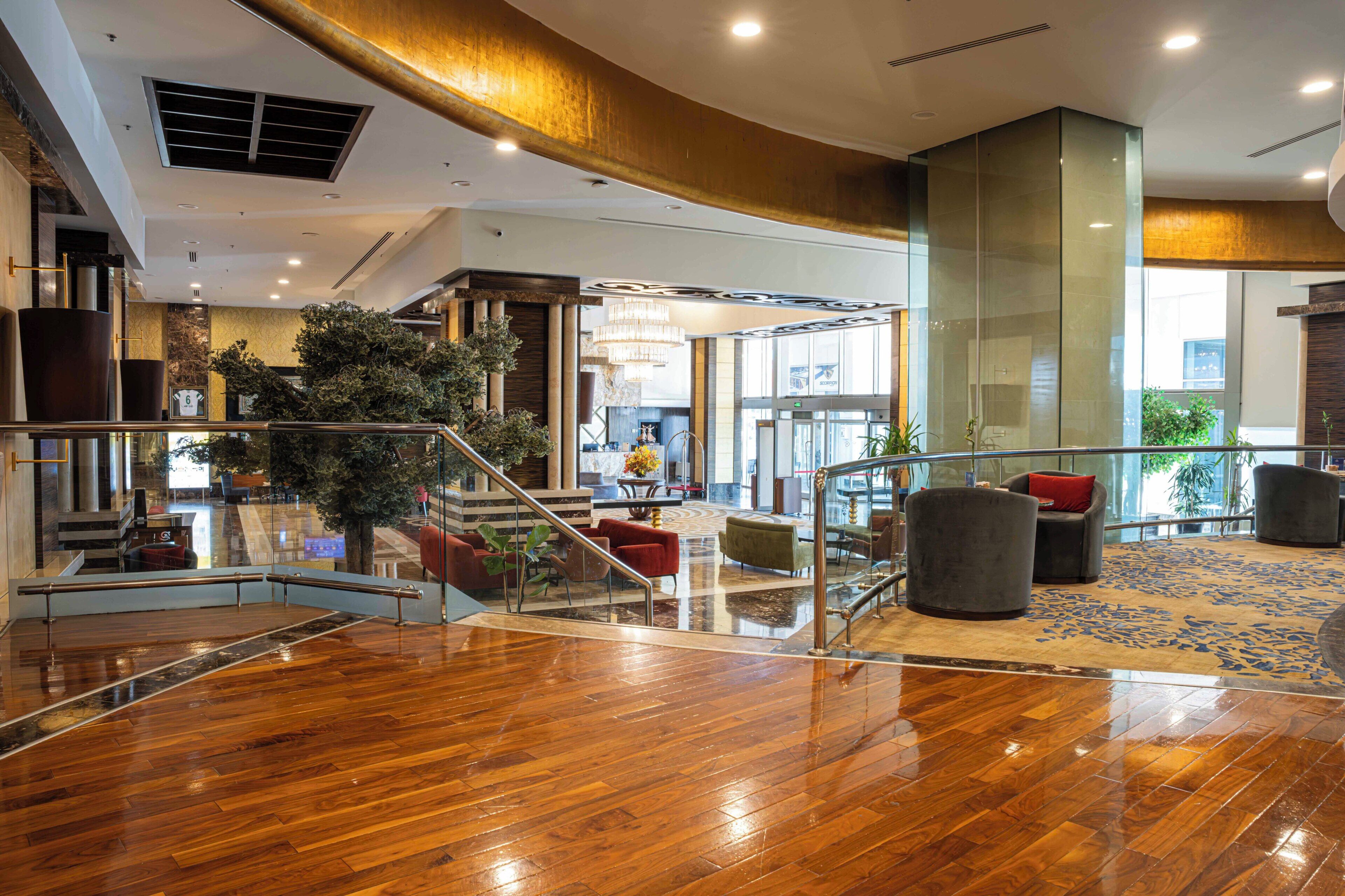 A spacious lobby with a wooden floor, a staircase, and a seating area with chairs and a sofa.