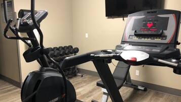 A gym with a treadmill, dumbbells, and a stationary bike.