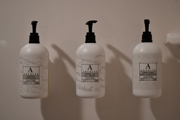 Tres botellas de champú y acondicionador 'Archive' sobre una pared.