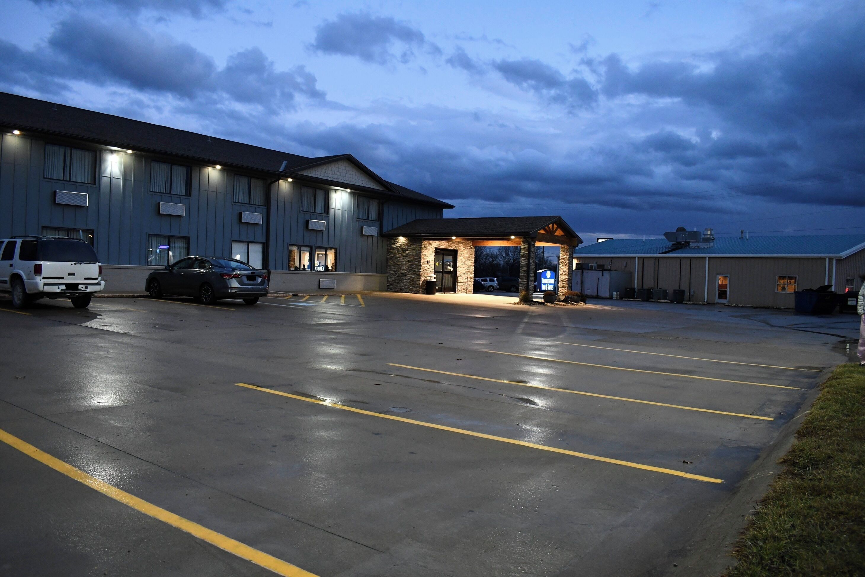 A hotel with a parking lot, a building entrance, and a view of the sky.