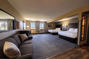 A hotel room with a large bed, a smaller bed, a sofa, a desk, and a TV.