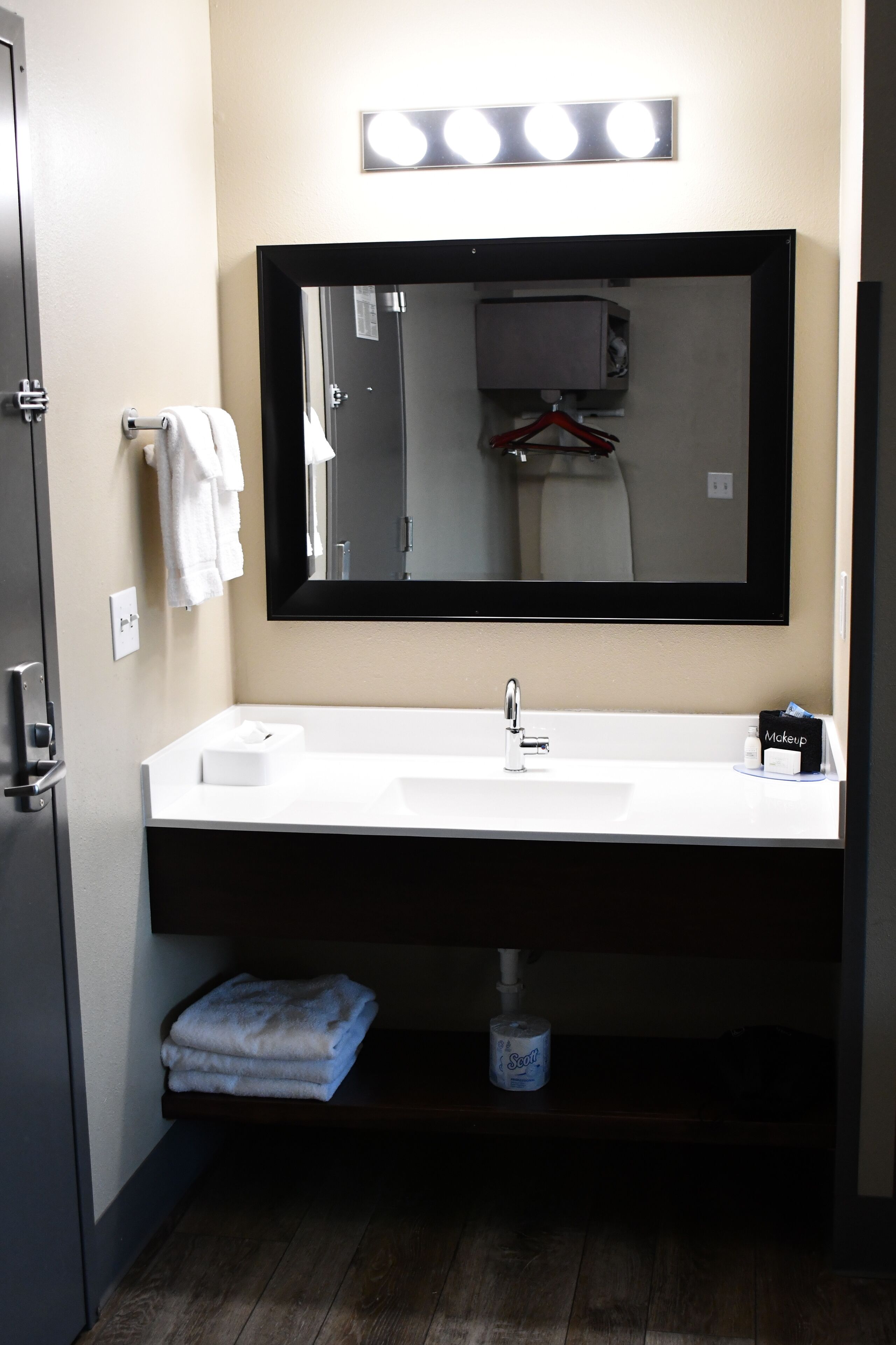 A bathroom with a white sink, a large mirror, and a shelf below the sink.