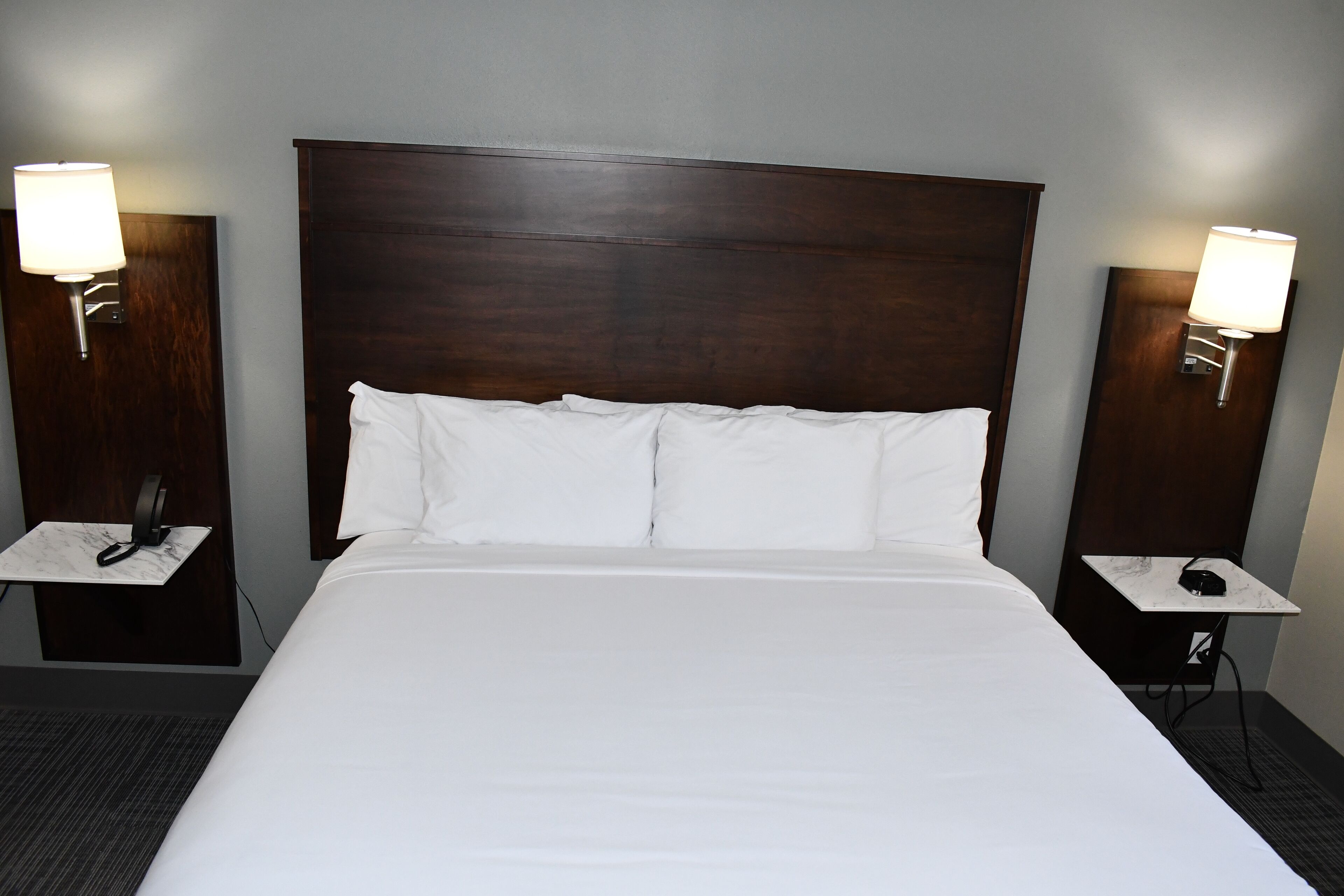 A hotel room with a large bed, two bedside tables, and two wall-mounted lamps.