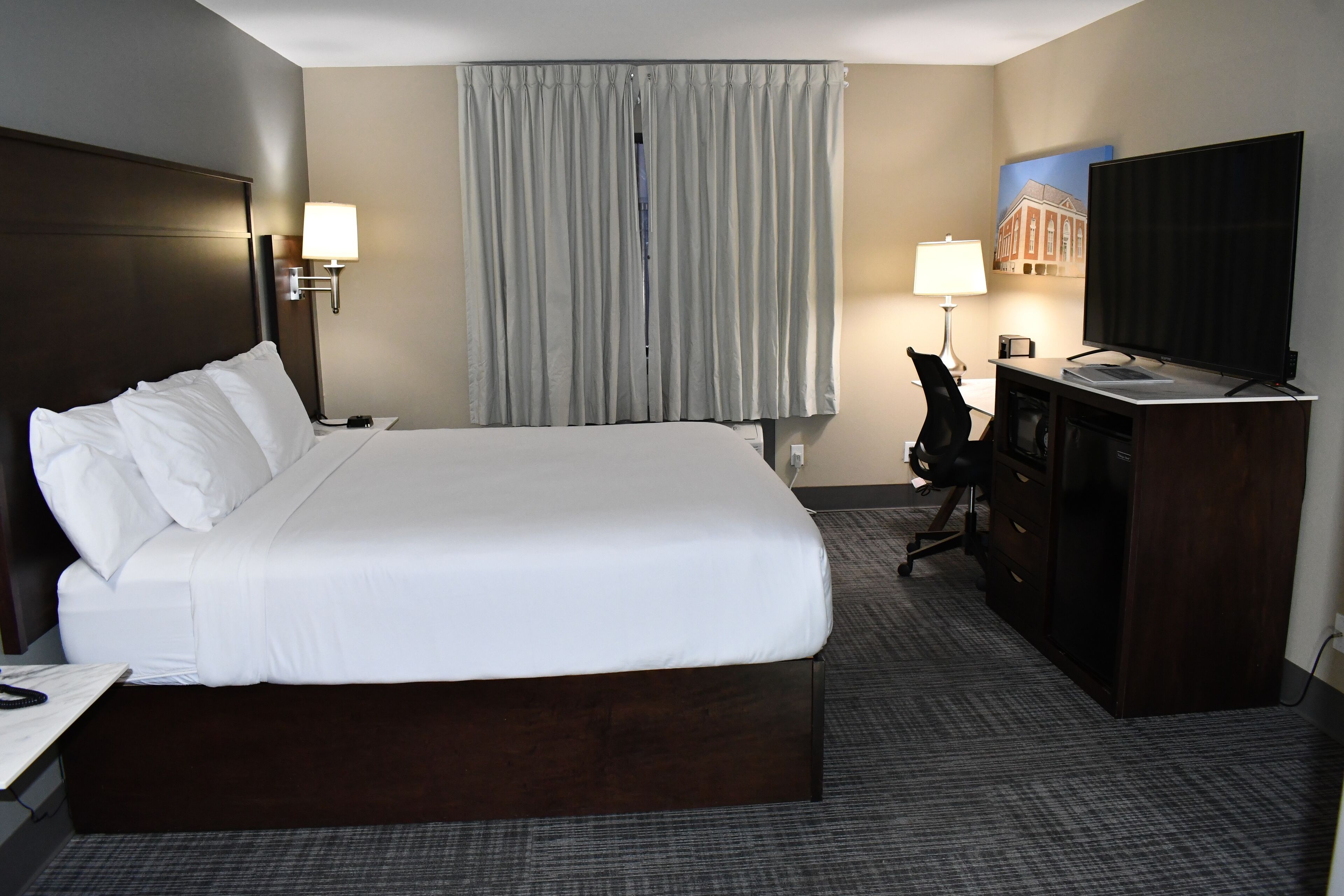 A hotel room with a large bed, a desk with a chair, a television, and a window with curtains.
