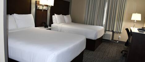 A hotel room with two beds, a desk, a chair, a lamp, and a window with curtains.