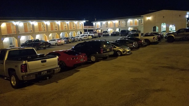 Un parking avec plusieurs voitures et un bâtiment dont les nombreuses fenêtres sont illuminées.