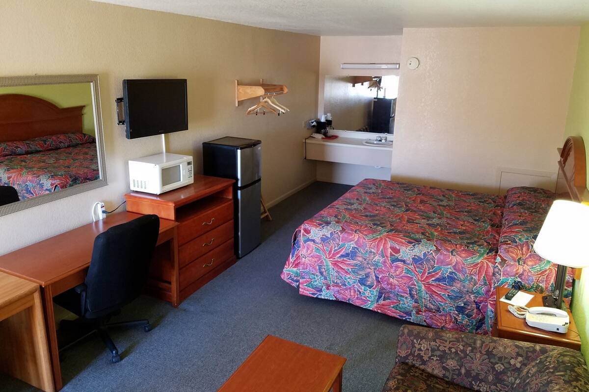 Une chambre d’hôtel comprenant un lit, un bureau avec un ordinateur, un réfrigérateur, un four à micro-ondes, une table de chevet avec une lampe et une commode.