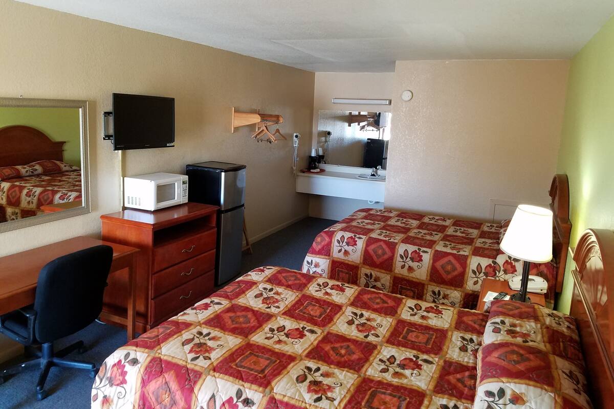 Une chambre d’hôtel avec deux lits, un bureau avec un ordinateur, un réfrigérateur, un four à micro-ondes, une télévision, un miroir et une table de chevet avec une lampe.
