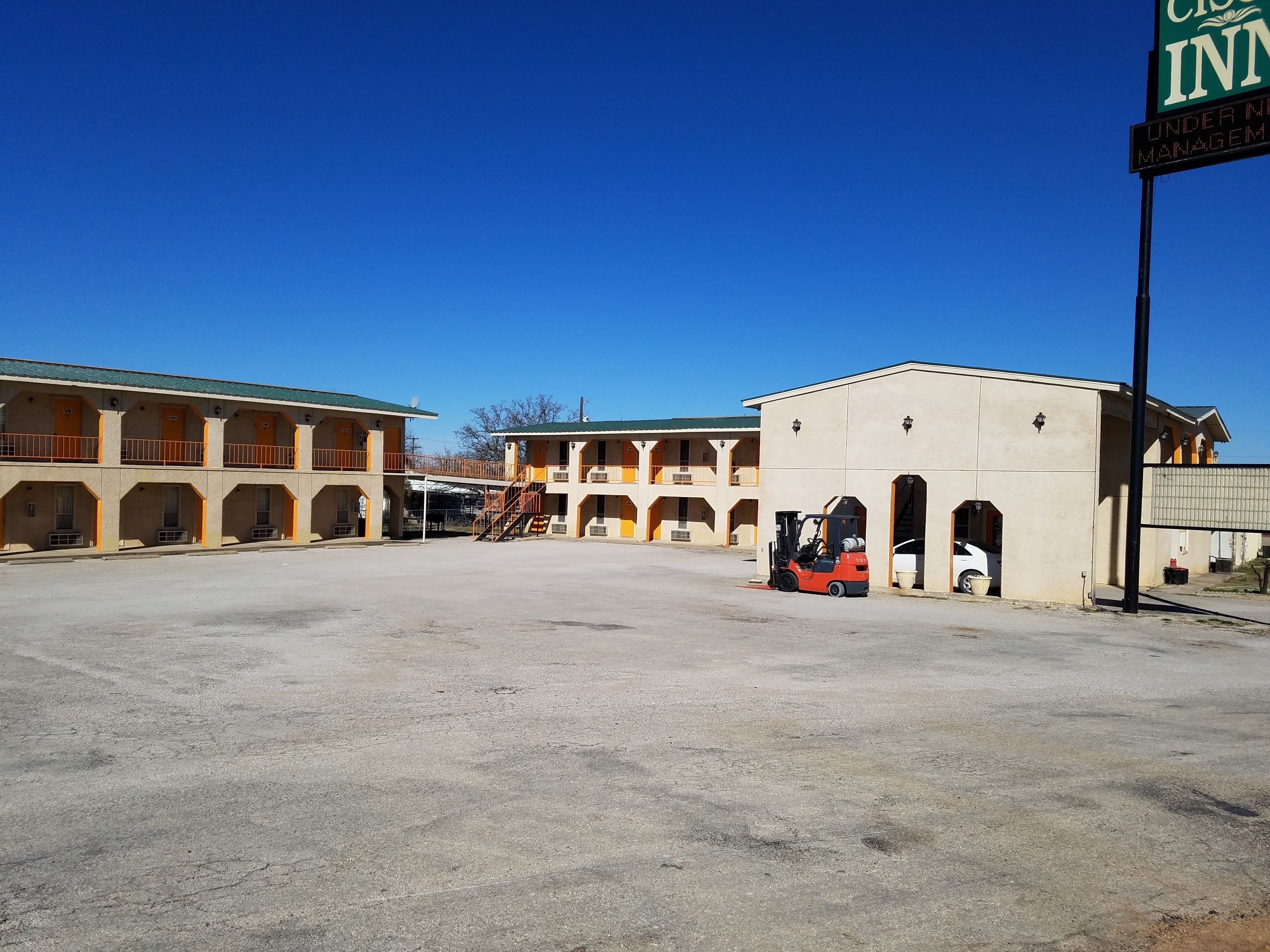 A motel with multiple buildings, a parking area, and a forklift.