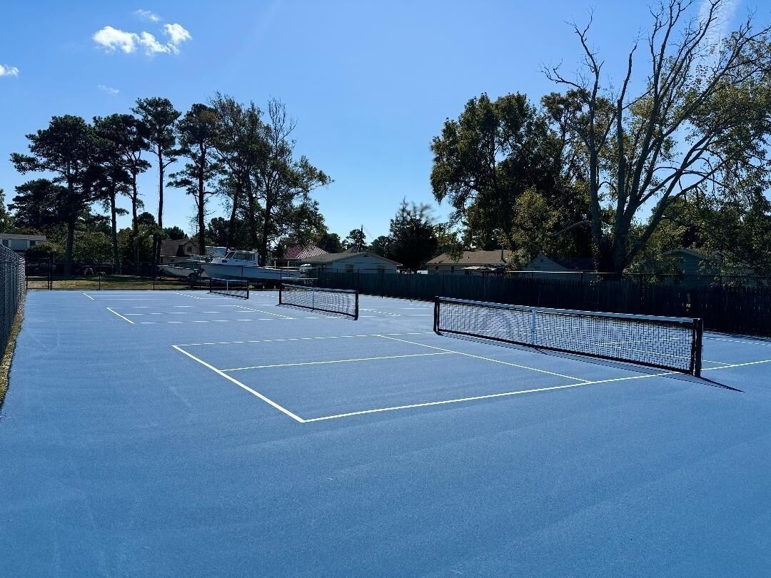 En tennisbane med net, omgivet af træer og bygninger.