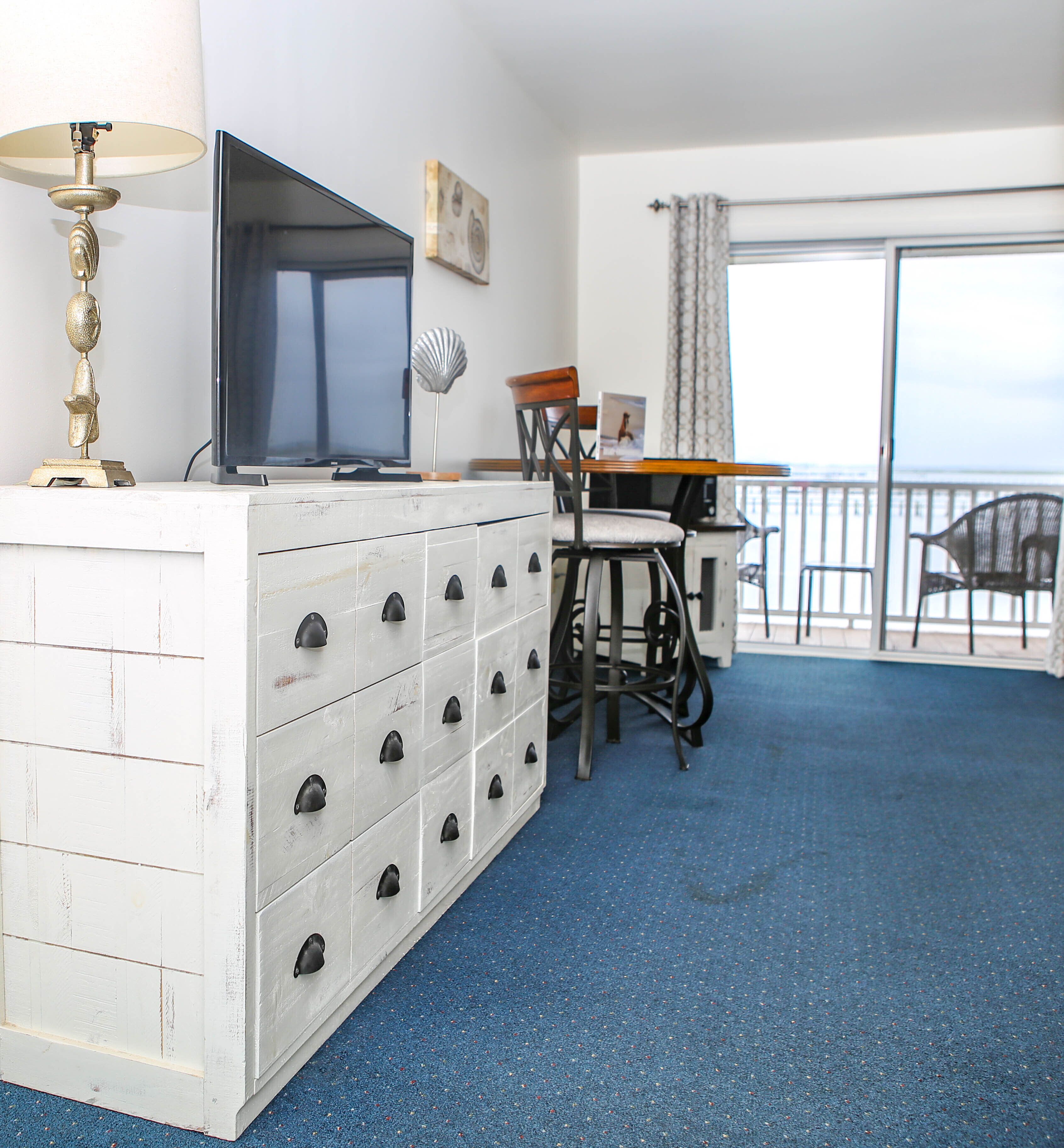 A room with a white dresser, a television, a chair, and a table.