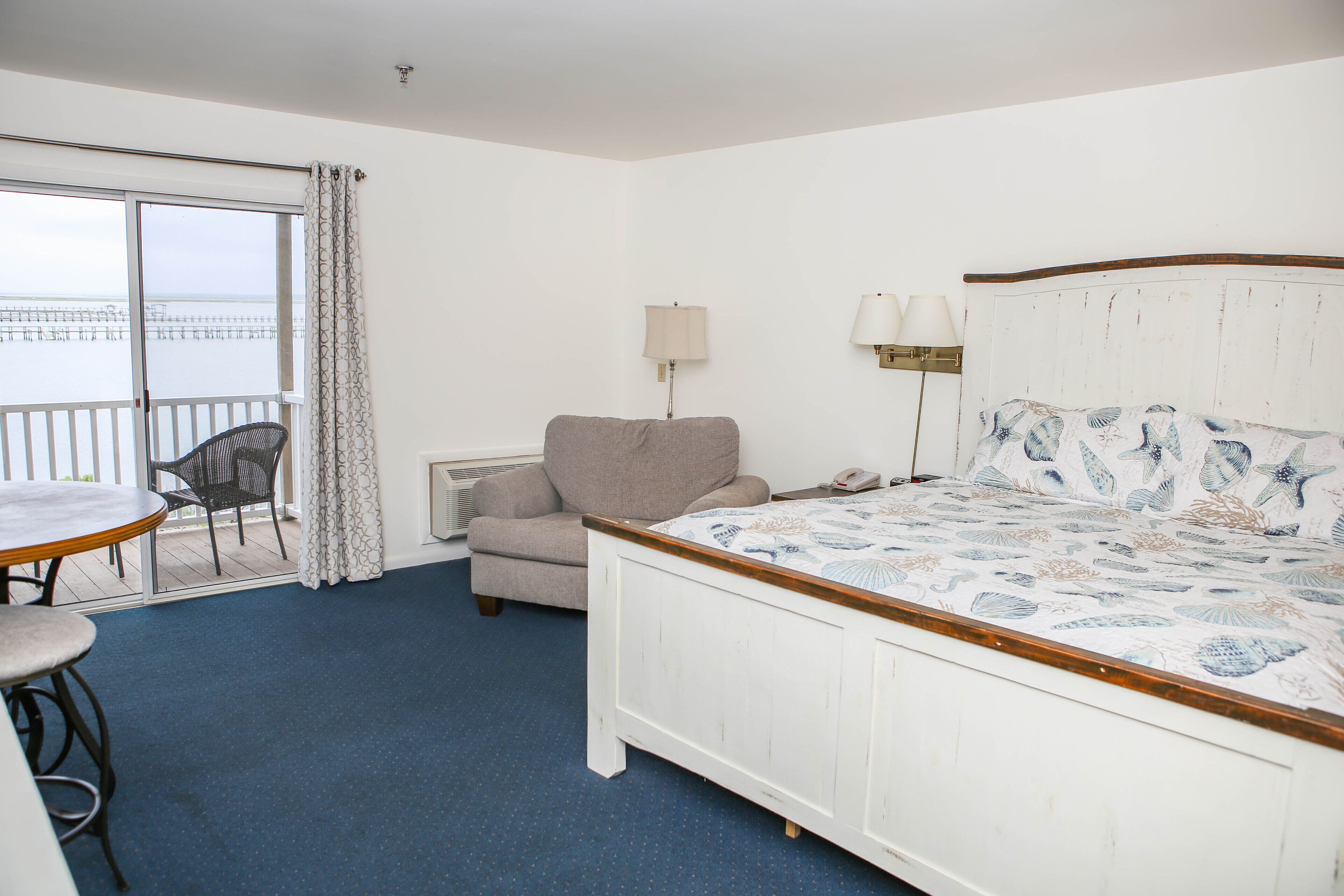Habitación de hotel con cama, una silla, una mesa y vistas al mar a través de una puerta corredera.