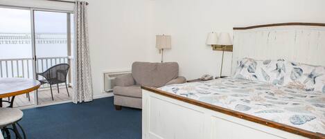 Habitación de hotel con cama, una silla, una mesa y vistas al mar a través de una puerta corredera.