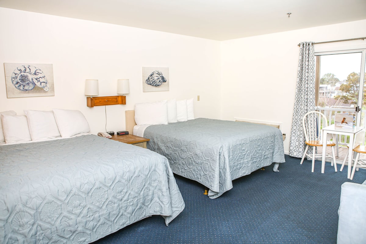 Ein Hotelzimmer mit zwei Betten, einem kleinen Tisch, Stühlen und Bildern an den Wänden.