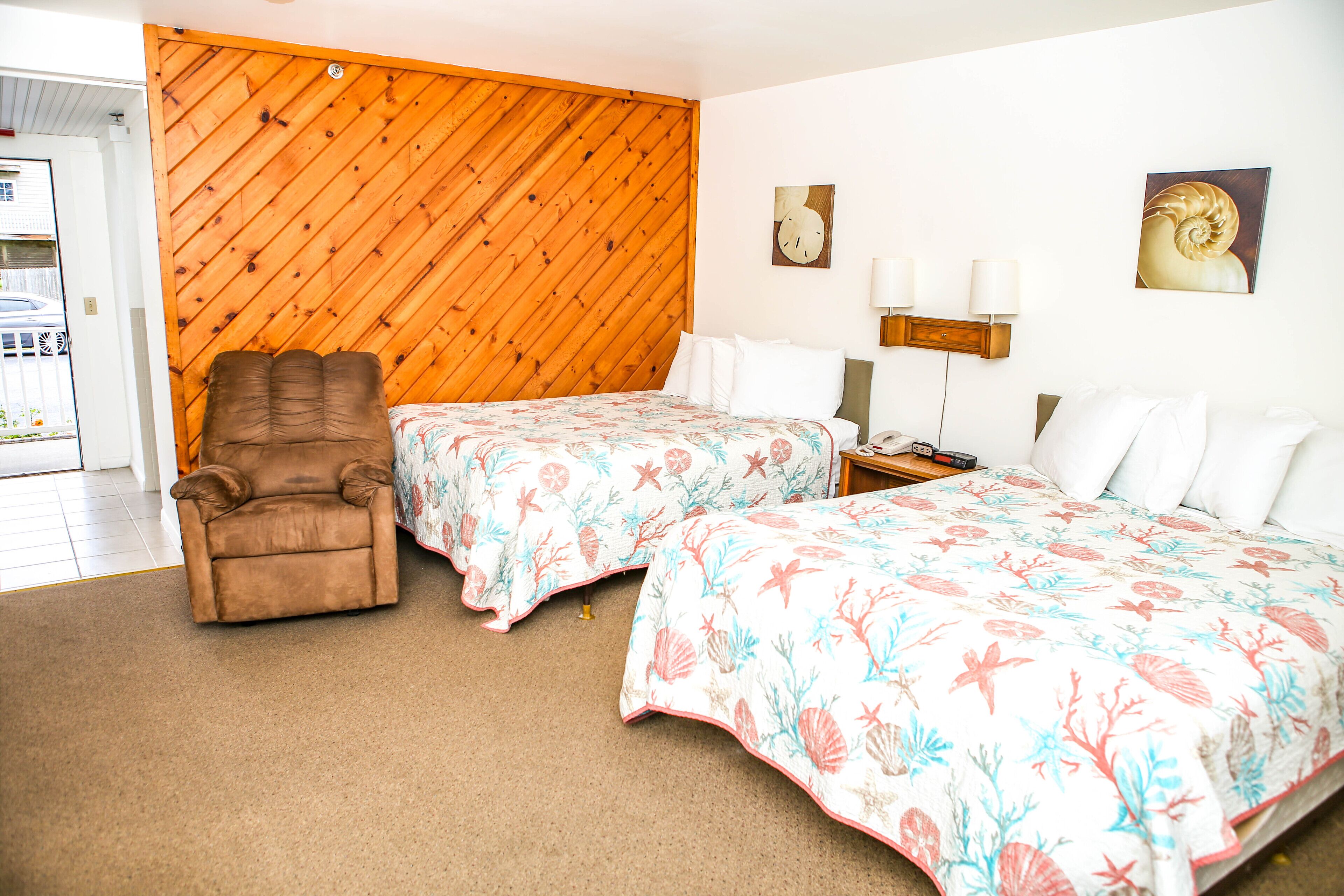 Ein Hotelzimmer mit zwei Betten, einem braunen Sessel, einer Holzvertäfelung und Bildern an den Wänden.