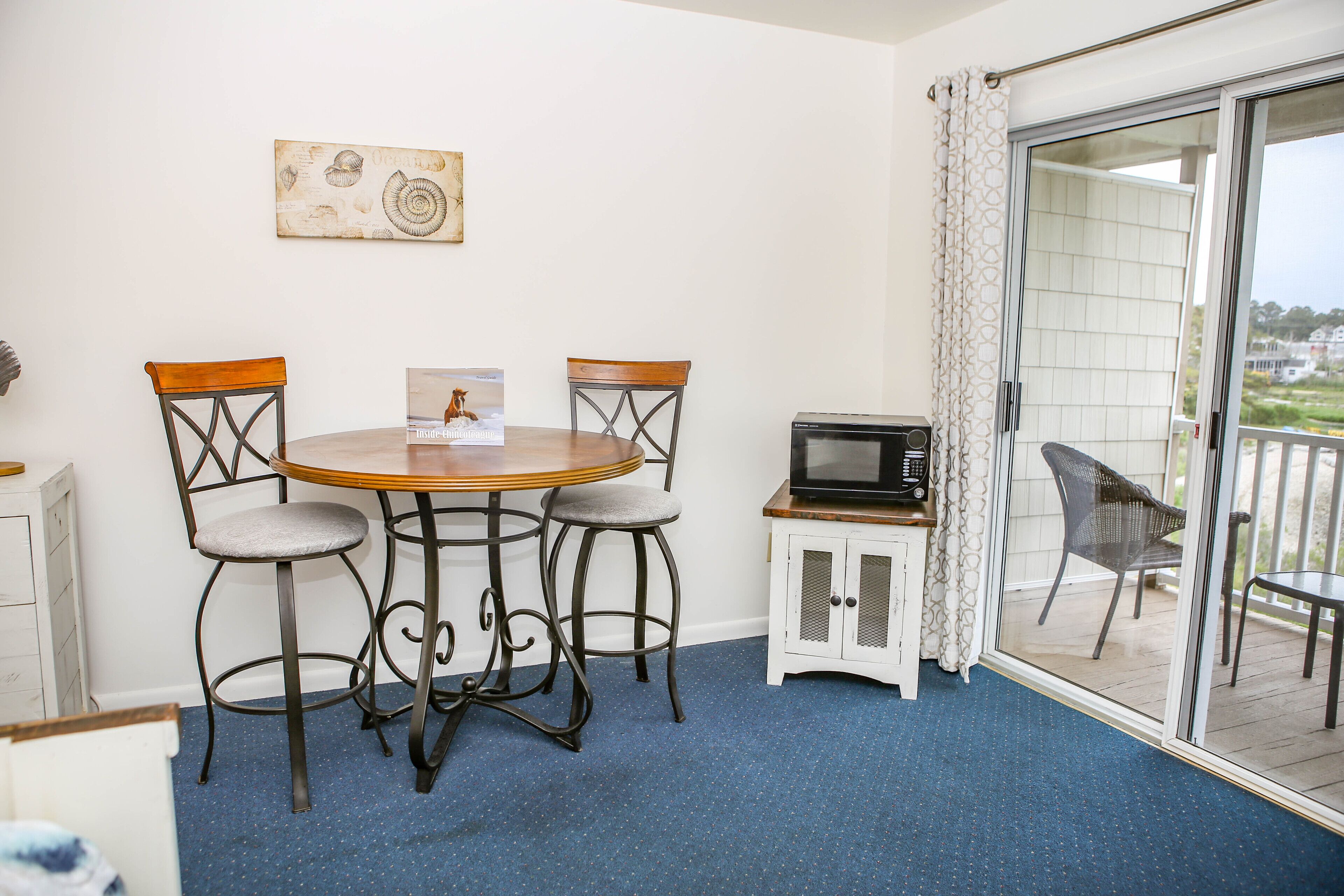 A balcony with a table and chairs, a microwave, and a view of the outdoors.