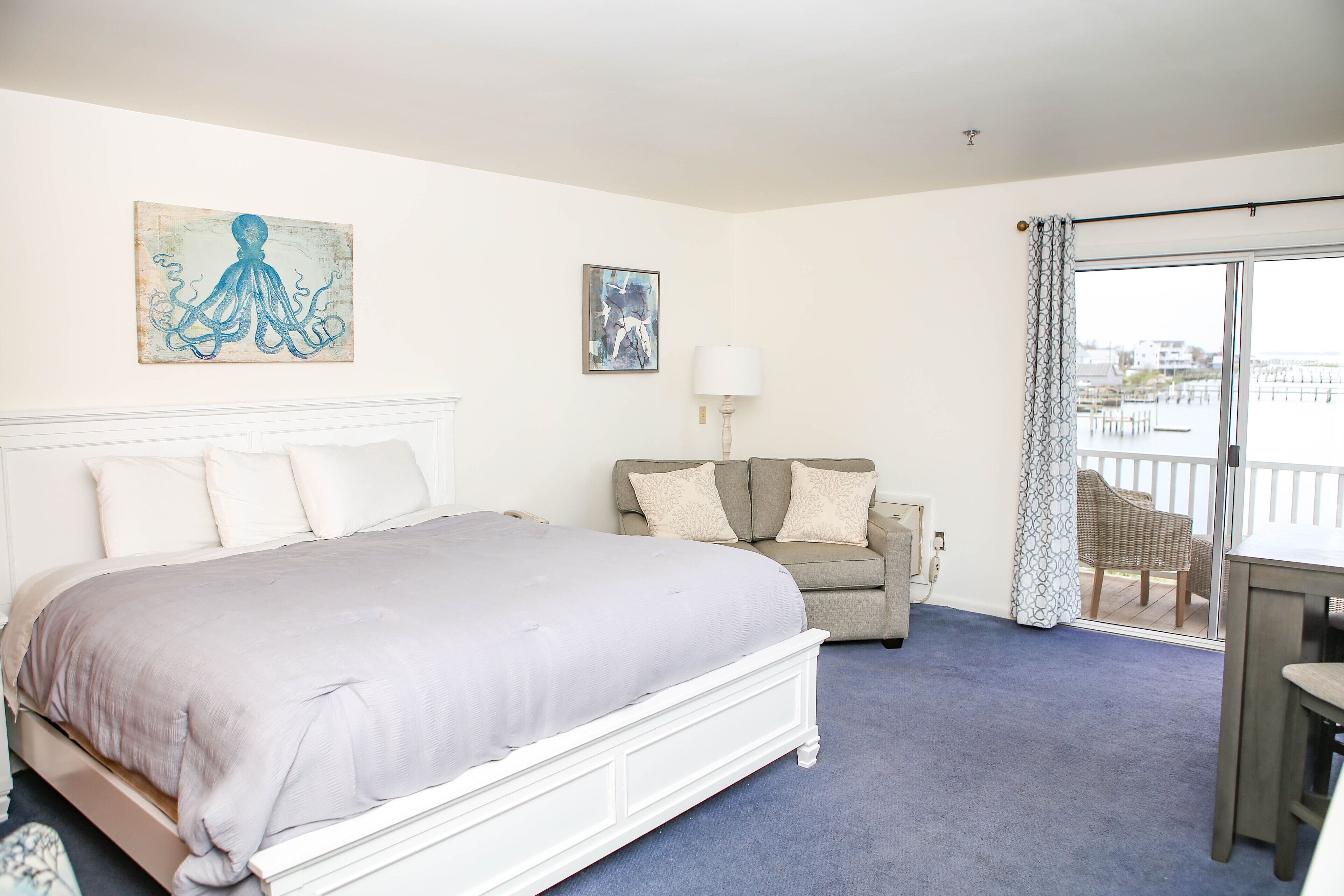 A hotel room with a large bed, a sofa, a table, and a view of the water.