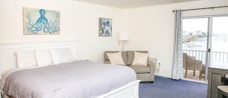 A hotel room with a large bed, a sofa, a table, and a view of the water.