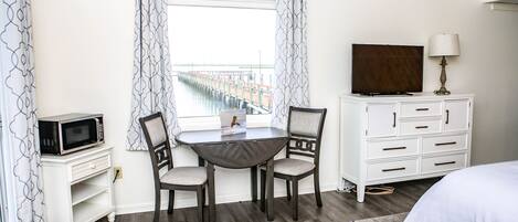 Une chambre d’hôtel équipée d’une table à manger, de deux chaises, d’un téléviseur, d’une commode et d’un tapis orné de motifs en forme d’étoiles.