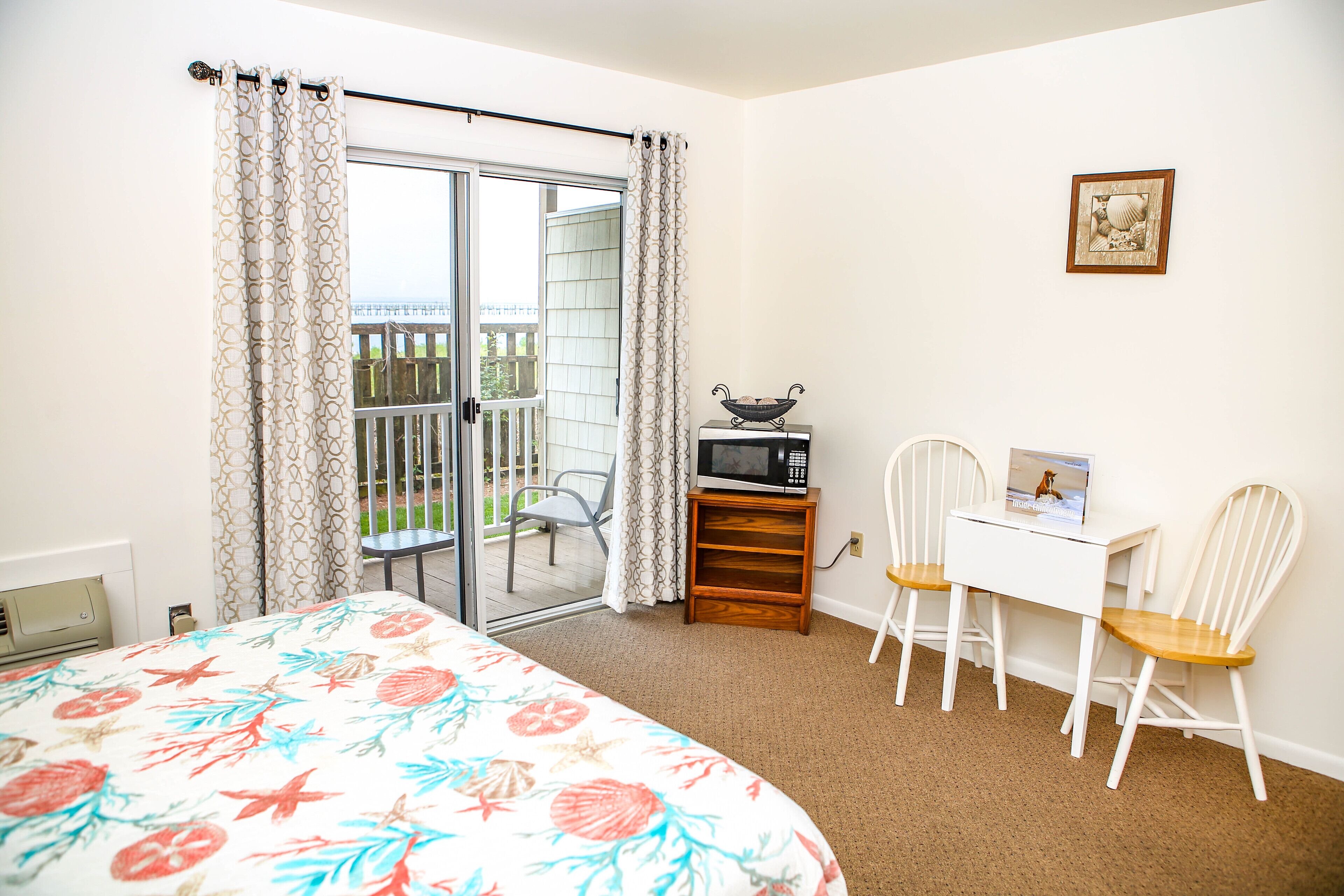 Ein Schlafzimmer mit einem Bett, einem Schreibtisch mit zwei Stühlen, einem Fernseher und einem Balkon mit einem Sessel.