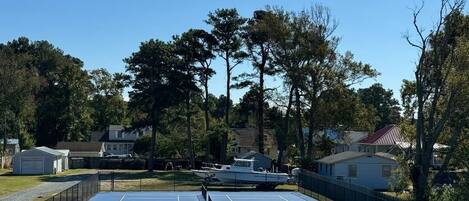 An outdoor tennis court with a net, surrounded by a fence, and houses in the background.